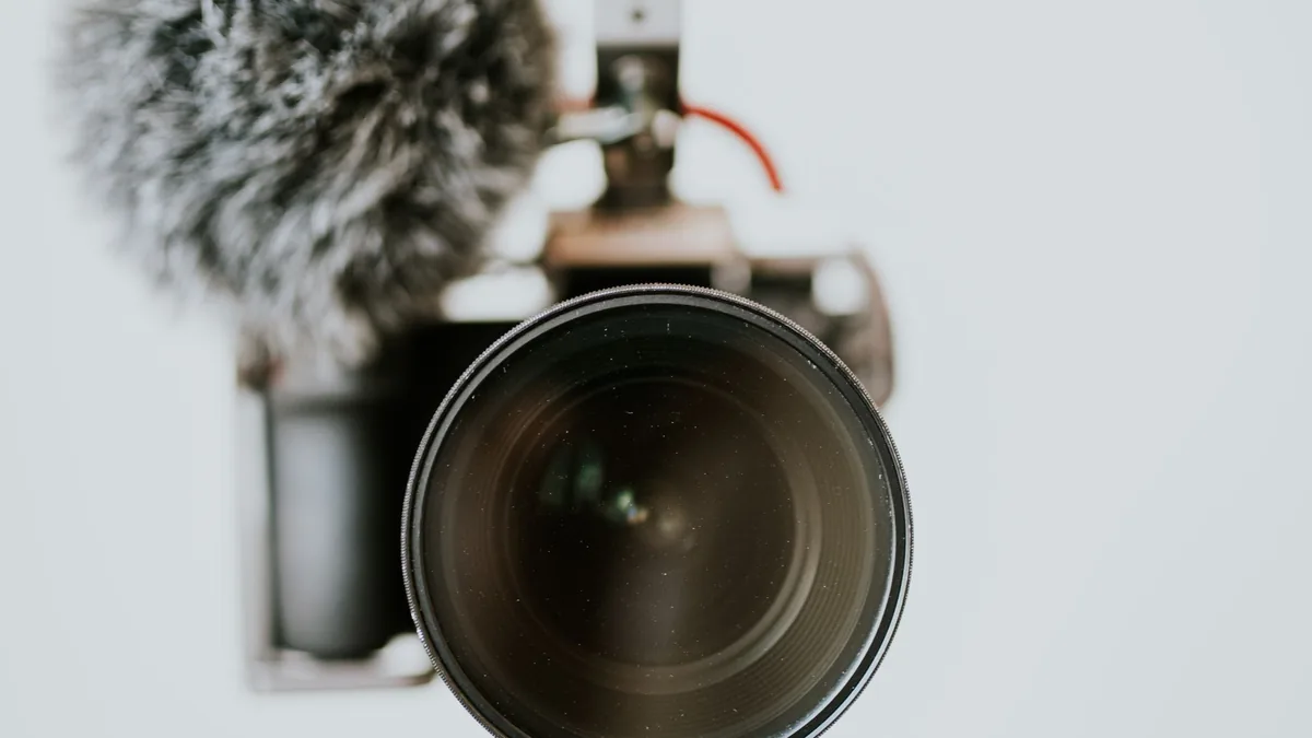 A DSLR camera with a furry microphone mounted on top, set up on a tripod for filming