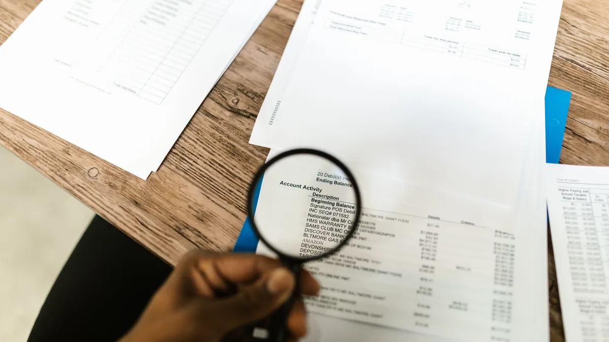 Reviewer holding a magnifying glass over a printed financial statement while buying an MSP