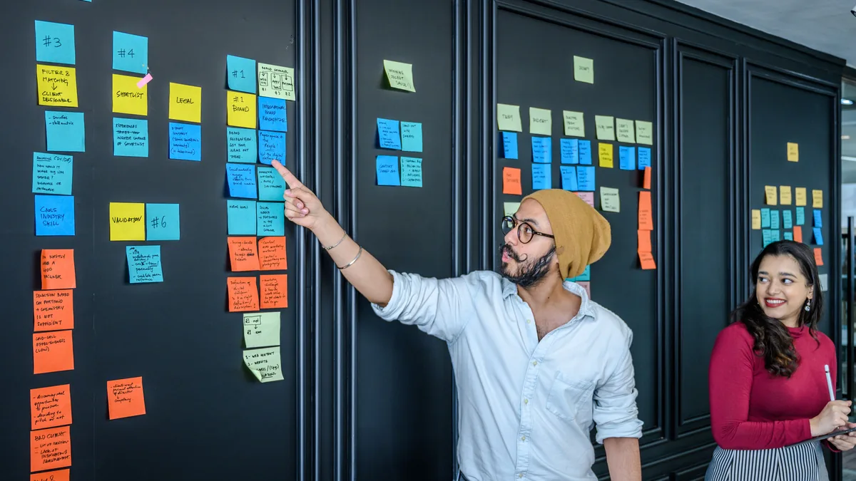 Two people organizing sticky notes on a wall to map out MSP service pages