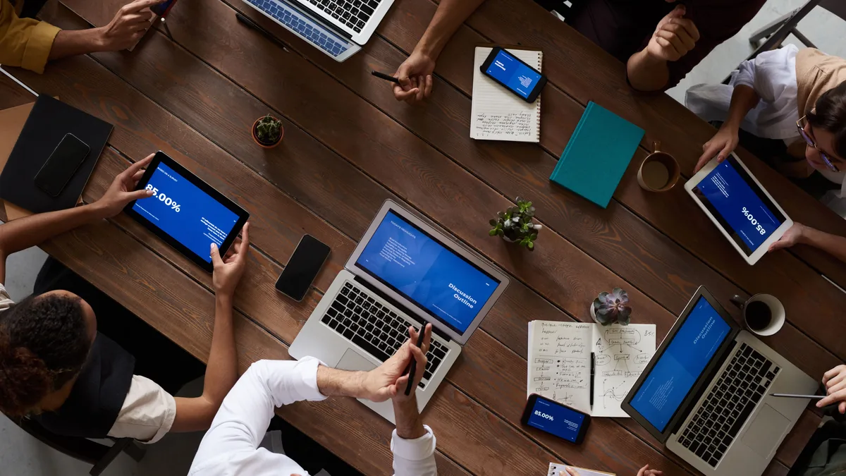 Overhead view of a team working around a table with laptops and tablets, reading and answering questions online